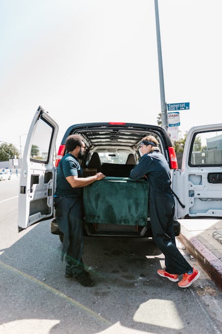 Two movers from Haringey Removals are standing inside a building, preparing for a home relocation in Wood Green. The female mover on the left is holding a cardboard box marked 'Fragile' with both hand